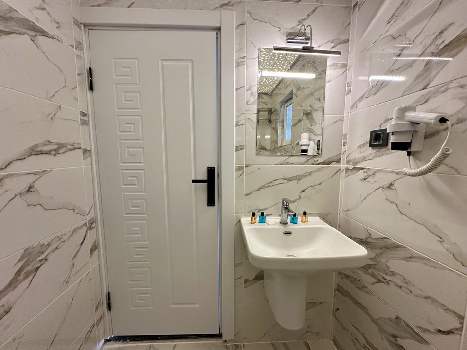 Banyoda kapı, lavabo, ayna ve saç kurutma makinesi.