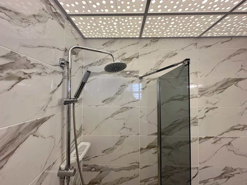 Cam duş kabini ve mermer desenli duş duvarları.