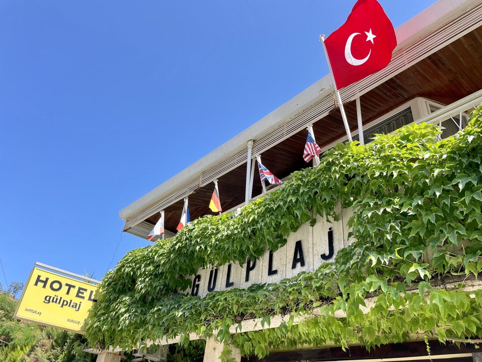 Türk bayrağı ve sarmaşıklarla otel giriş cephesi.