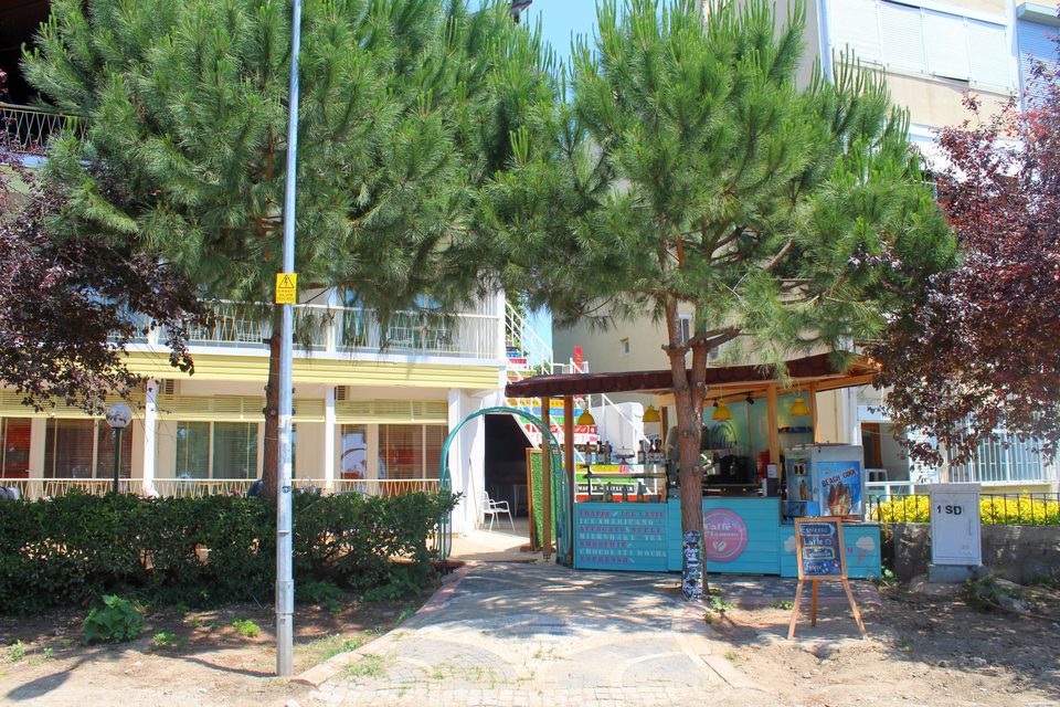 Otelin ağaçlı ön cephesi ve kafe girişi.