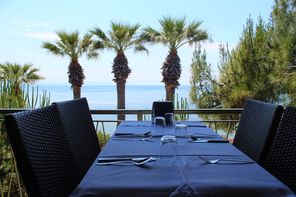 Deniz ve palmiye manzarası önünde hazırlanmış restoran masası.